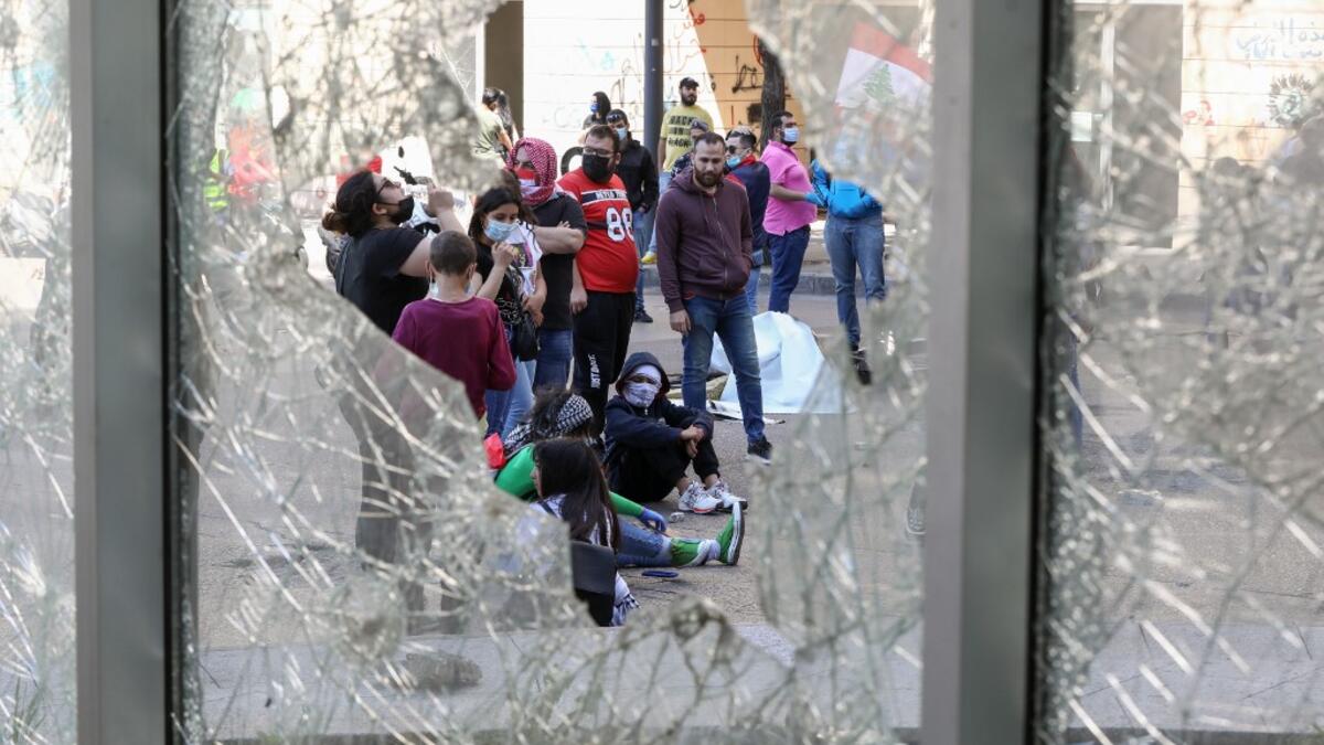 Lebanese anti-government protesters, some wearing protective masks amid the COVID-19 pandemic, are seen through a broken store window during a demonstration against the growing economic hardship in downtown Beirut on May 1, 2020, marking International Workers' Day (Labour Day). ANWAR AMRO / AFP
