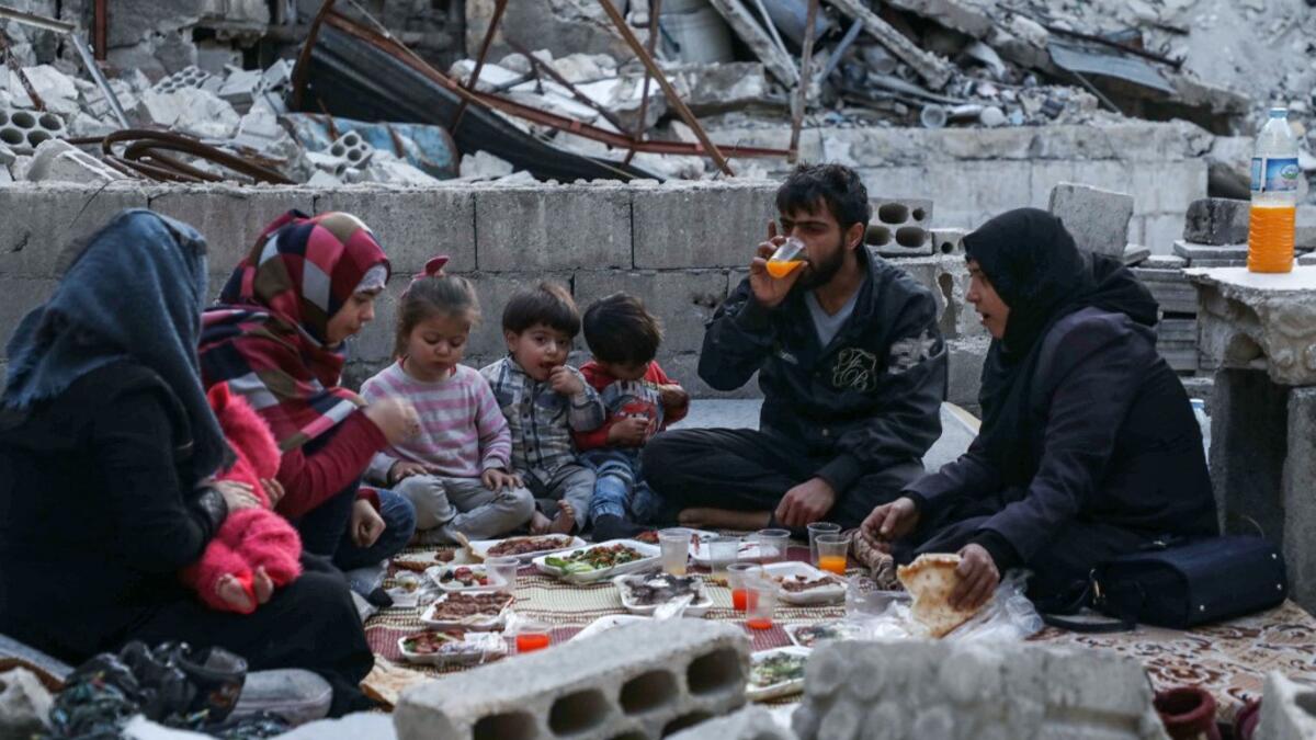 This picture taken on May 4, 2020 during the Muslim holy fasting month of Ramadan shows Tareq Abu Ziad (L), a displaced Syrian from the town of Ariha in the southern countryside of the Idlib province, smoking as members of his family break their fast together for the sunset "iftar" meal, in the midst of the rubble of their destroyed home upon their return to the town for one day after fleeing during the previous military assault by Syrian government forces and their allies. AAREF WATAD / AFP
