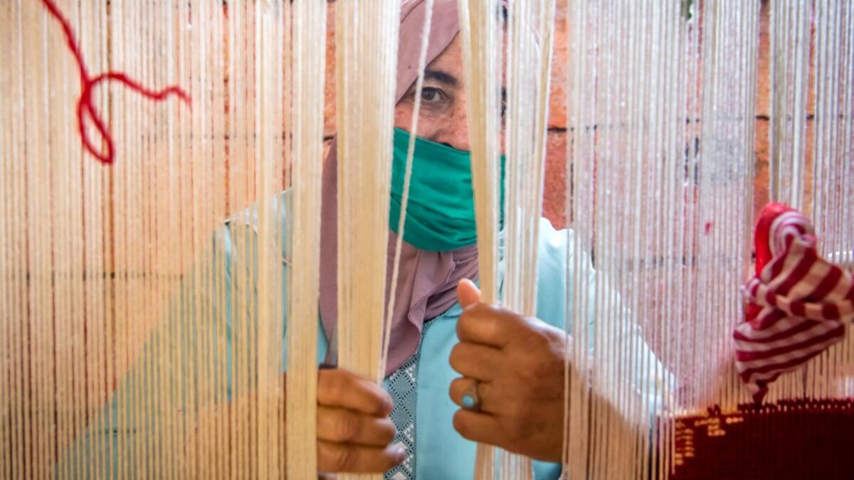 A Moroccan rug weaver peeks from behind carpet thread at a workshop in the city of Sale, north of the capital Rabat, on June 3, 2020, during the novel coronavirus pandemic. Artisans in Morocco have been starved of income for almost three months because of the COVID-19 pandemic. The crafts industry represents some seven percent of GDP, with an export turnover last year of nearly 1 billion dirhams ($100 million). FADEL SENNA / AFP