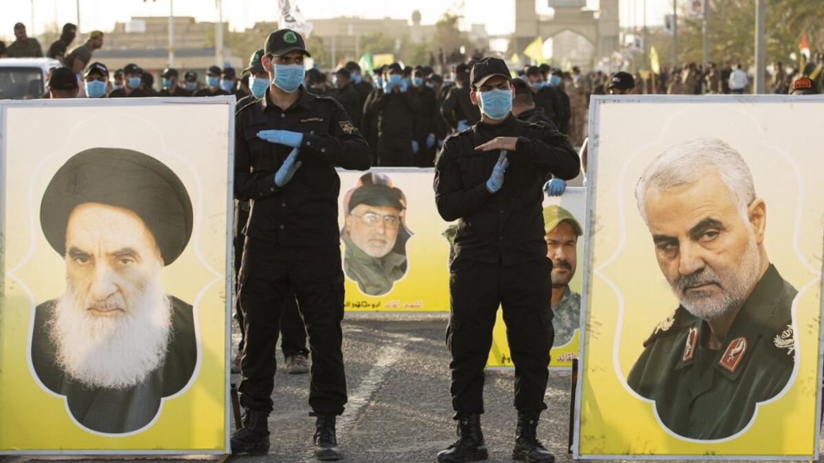 Members of the Hashed al-Shaabi (Popular Mobilisation) paramilitary force stand near portraits of Iraq's top Shiite cleric Grand Ayatollah Ali Sistani (L) and slain Iranian general Qasem Soleimani (R) during a military parade in the southern Iraqi city of Basra on June 14, 2020, marking the sixth anniversary of its founding after Sistani called to defend the country from the Islamic State group (IS). Hussein FALEH / AFP