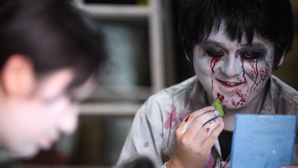 This picture taken on June 15, 2020 shows actor Kenta Iwana (R), 25, putting on zombie makeup before a demonstration of a drive-in haunted house at a garage in Tokyo. A car horn beeps and the horror begins: a bloody murder and rampaging zombies. But this drive-in haunted house in Japan protects against the most terrifying enemy of all -- coronavirus. Inside a car, guests can scream as loudly as they like, with no mask required, as hideous creatures daubed in blood swarm towards them.  Philip FONG / AFP