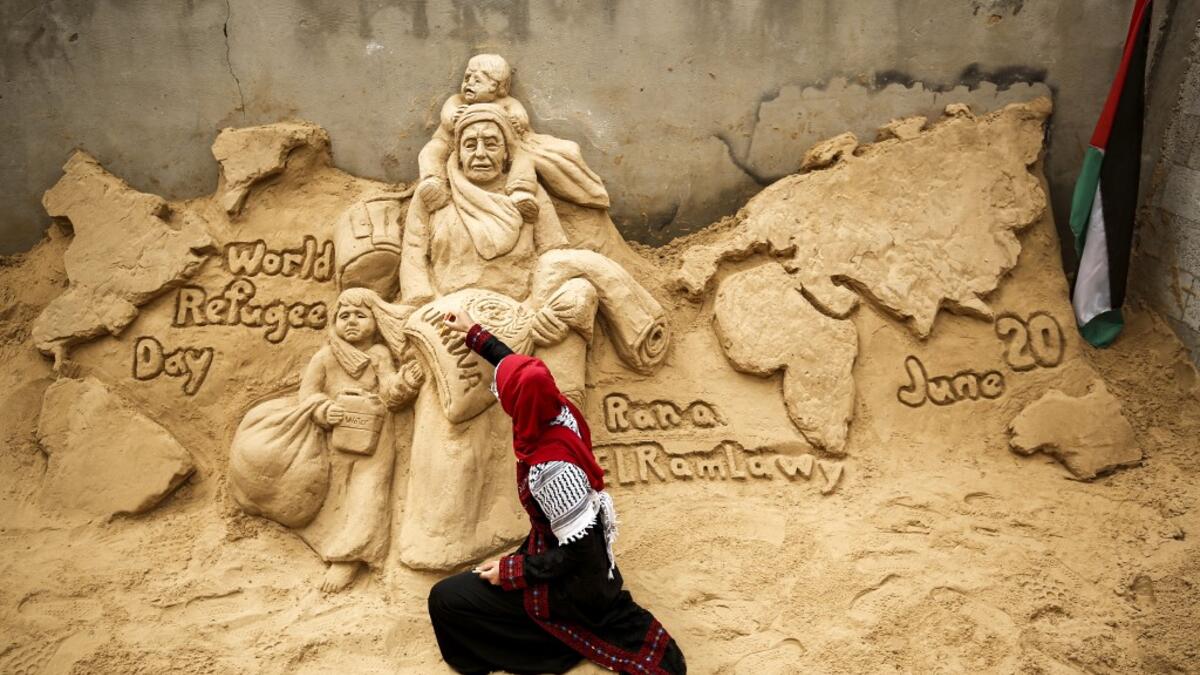 Palestinian sand sculptor Rana Ramlawi finishes a new artwork creation commemorating World Refugee Day, a day dedicated by the United Nations General Assembly to raising awareness of the situation of refugees throughout the world, in Gaza City on June 20, 2020, depicting a woman carrying a child and a sack of flour bearing the logo of the United Nations Relief and Works Agency for Palestine Refugees (UNRWA). MOHAMMED ABED / AFP