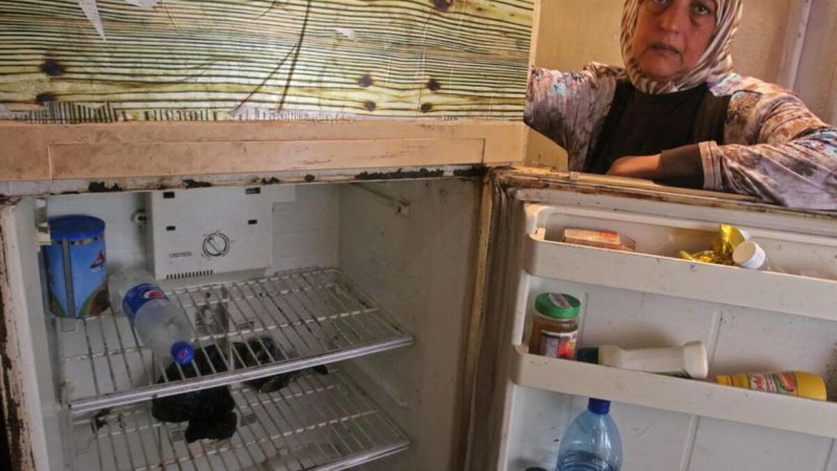 Holding her fridge door open, Fadwa Merhebi explains she already downsized once because she could not afford enough food to fill it up. Now it contains only a bottle of mineral water and two cucumbers. | A Lebanese woman displays the content of her refrigerator. Image Credit: AFP