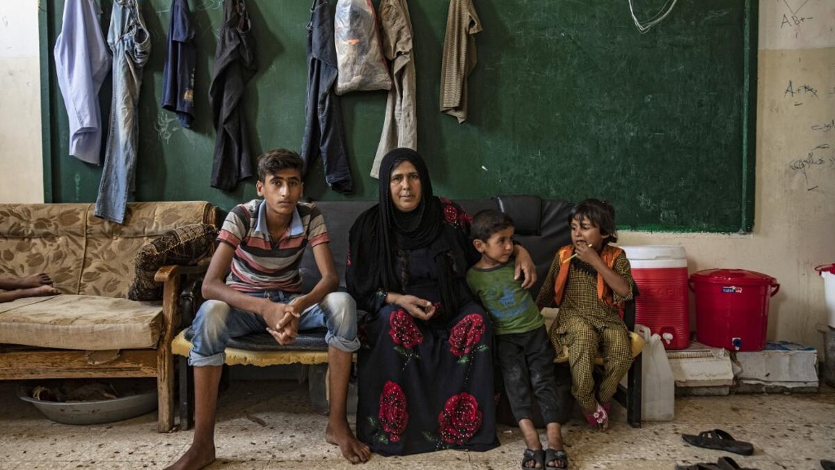 A woman sits with children as they pose for a picture at a former classroom in a school building where Syrians -- displaced from the area of Ras al-Ain by the Turkish offensive on the northeast -- are staying in the city of Hasakah, on June 30, 2020. Delil SOULEIMAN / AFP