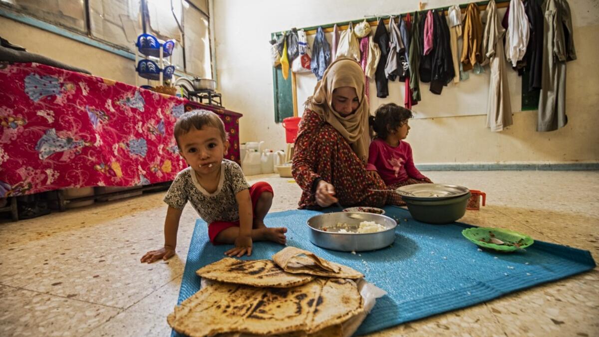 A woman feeds a child while sitting on the floor at a former classroom in a school building where Syrians -- displaced from the area of Ras al-Ain by the Turkish offensive on the northeast -- are staying in the city of Hasakah, on June 30, 2020. Delil SOULEIMAN / AFP
