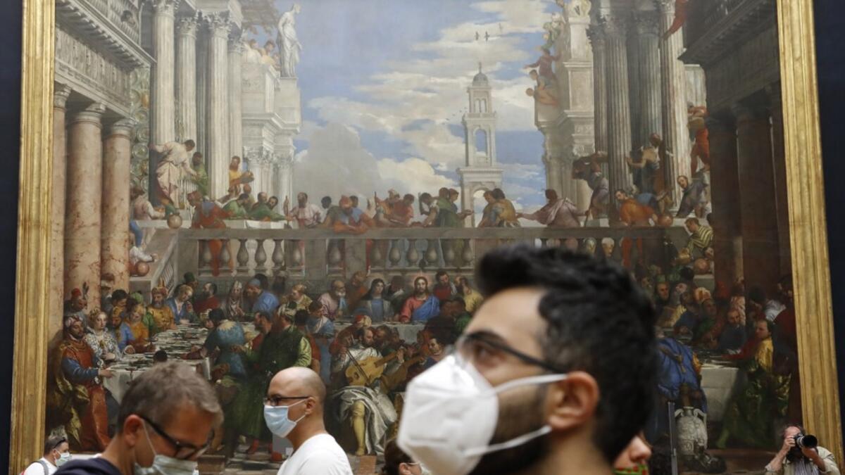 Visitors wearing face mask stands in front of " The Wedding Feast at Cana " oil on canvas painting by the Italian artist Paolo Veronese (1528–1588) at the Louvre Museum in Paris on July 6, 2020, on the museum' s reopening day.FRANCOIS GUILLOT / AFP