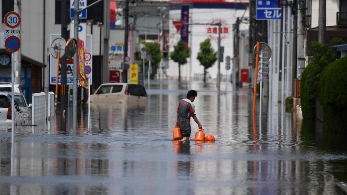 A worker wades through flood waters as he delivers gas bottles in Kurume, in Fukuoka Prefecture on July 8, 2020. Japan will deploy more troops to search for survivors of devastating floods and landslides that have killed at least 52 people in the southwest of the country, Prime Minister Shinzo Abe pledged CHARLY TRIBALLEAU / AFP