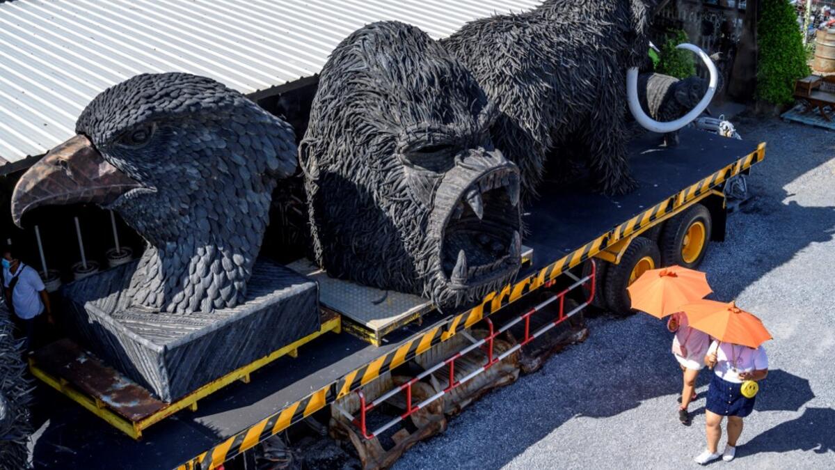 This photograph taken on July 18, 2020 shows tourists walking in front of giant sculptures of animals made of used car tyres at the Ban Hun Lek museum in Ang Thong, some 100km north of Bangkok. "Ban Hun Lek" or "The House of Steel Robots" is a museum where a collective of artists display their scrap metal creations depicting popular comics and sci-fi film characters. Mladen ANTONOV / AFP