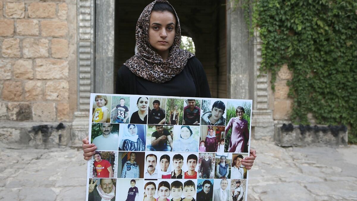 Yazidi woman Ashwaq Haji, allegedly used by the Islamic State group (IS) as a sex slave, holds portraits of jihadists' victims from her village of Kocho near Sinjar, as she visits the Lalish temple, in Lalish, northern Iraq, on August 15, 2018. - A young Yazidi woman who fled to Germany but returned home to northern Iraq says she cannot escape her Islamic State group captor who held her as a sex slave for three months. Ashwaq Haji, 19, says she ran into the man in a German supermarket in February. Traumatis