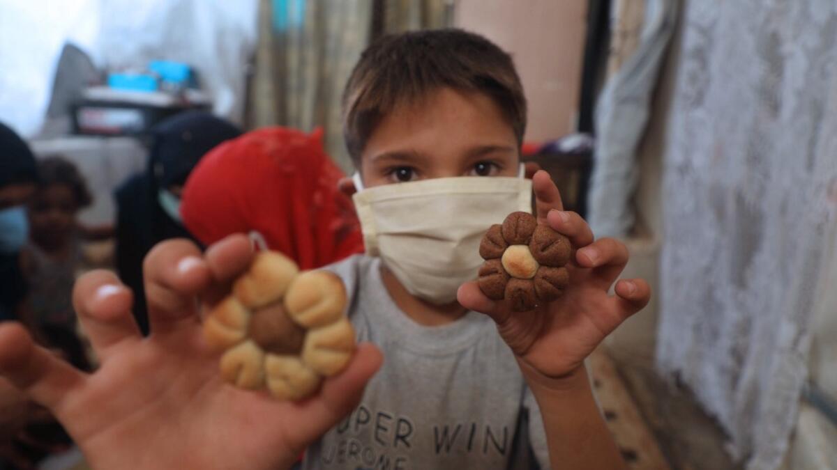 A displaced Syrian boy, wearing protective a face mask, displays cookies to the camera at a camp for the internally displaced near the town of Sarmada in Syria's northwestern Idlib province on July 29, 2020, as Muslims across the world are getting ready to celebrate Eid al-Adha. AAREF WATAD / AFP