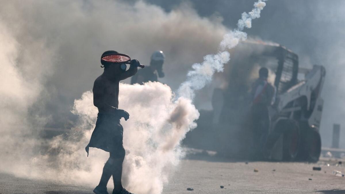 A topless protester wearing a gas mask uses a racket to volley back a tear gas canister during clashes with security forces in downtown Beirut on August 8, 2020, following a demonstration against a political leadership they blame for a monster explosion that killed more than 150 people and disfigured the capital Beirut. PATRICK BAZ / AFP