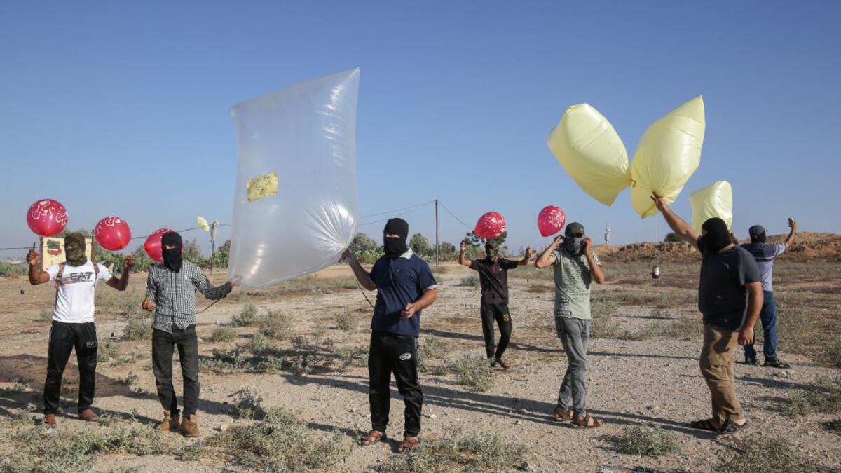 Palestinians stand holding inflated balloons and plastic bags attached with incendiary devices to be directed and flown towards Israel, near Rafah along the border between the Gaza Strip and Israel on August 21, 2020. SAID KHATIB / AFP