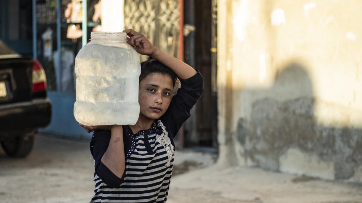 A Syrian girl carries a pot of water filled up from cisterns provided by humanitarian organisations during a water outage in Syria's northeastern city of Hasakah on August 22, 2020. As coronavirus spreads across northeast Syria, residents in Hasakeh have been caught up in the latest spat between Turkish forces to the north and Syrian Kurds it views as "terrorists". In October last year, Turkish forces occupied a 120-stretch (70-mile) stretch of land inside the Syrian border, including the Alouk power statio