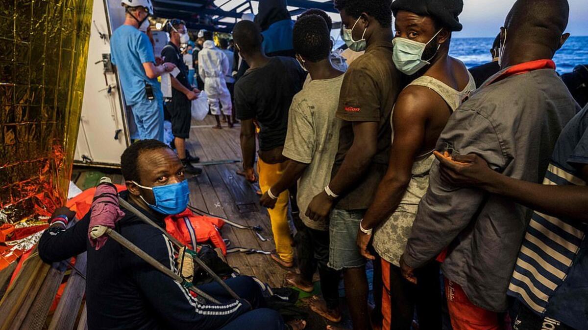 Migrants who have just been helped off the Louise Michel queue to see crew members and doctors including an injured man with crutches (AFP)