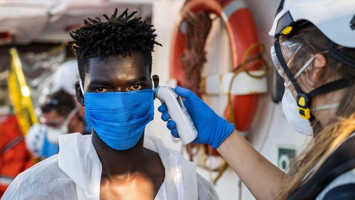 A crew member takes the temperature of a migrant  who has just been helped off Banksy's ship who is wearing protective clothes and a face mask (AFP)