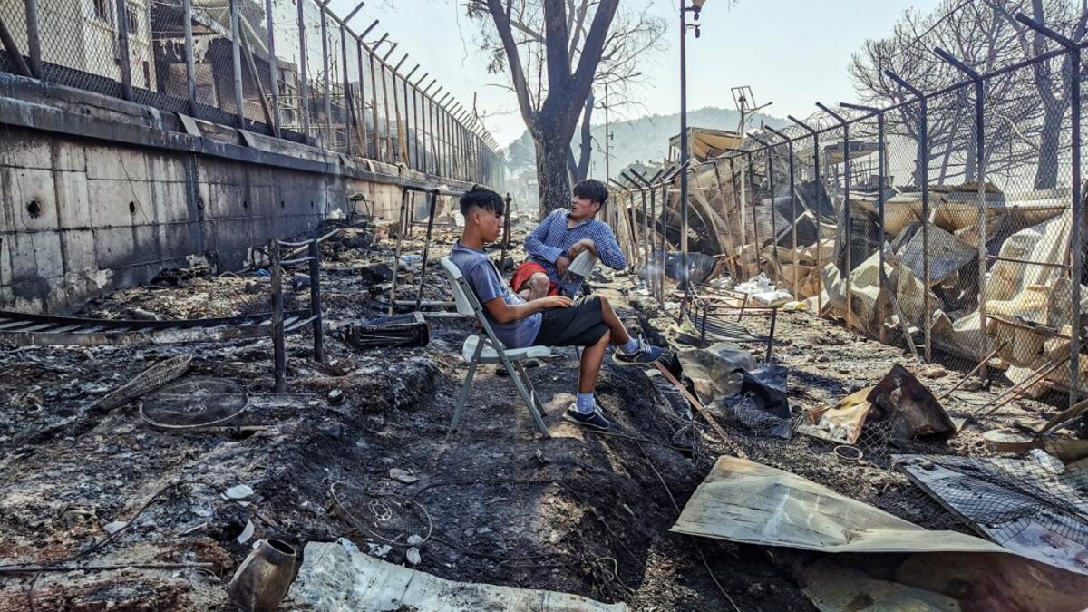Migrants sit inside the burnt Moria Camp on the Greek island of Lesbos on September 9, 2020, after a major fire. Thousands of asylum seekers on the Greek island of Lesbos fled for their lives early September 9, as a huge fire ripped through the camp of Moria, the country's largest and most notorious migrant facility. Over 12,000 men, women and children ran in panic out of containers and tents and into adjoining olive groves and fields as the fire destroyed most of the overcrowded, squalid camp.