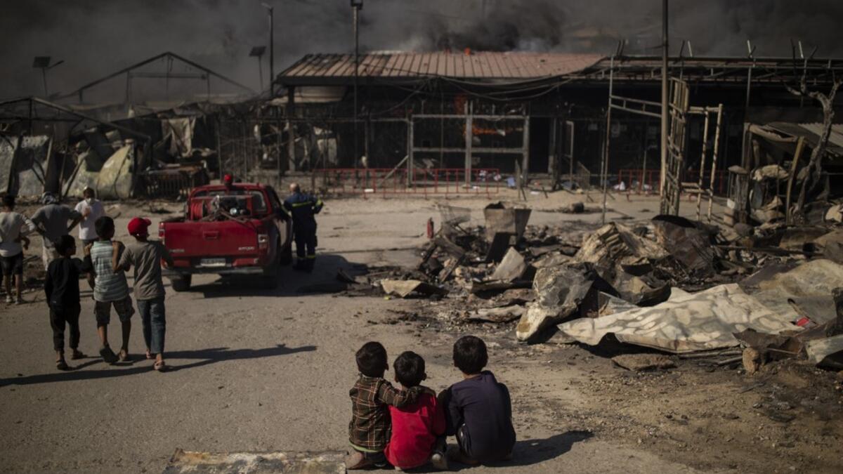 Children sit on the ground in the burnt camp of Moria on the island of Lesbos after a major fire broke out, on September 9, 2020. Thousands of asylum seekers on the Greek island of Lesbos fled for their lives on September 9, 2020 as a huge fire ripped through the camp of Moria, the country's largest and most notorious migrant facility.