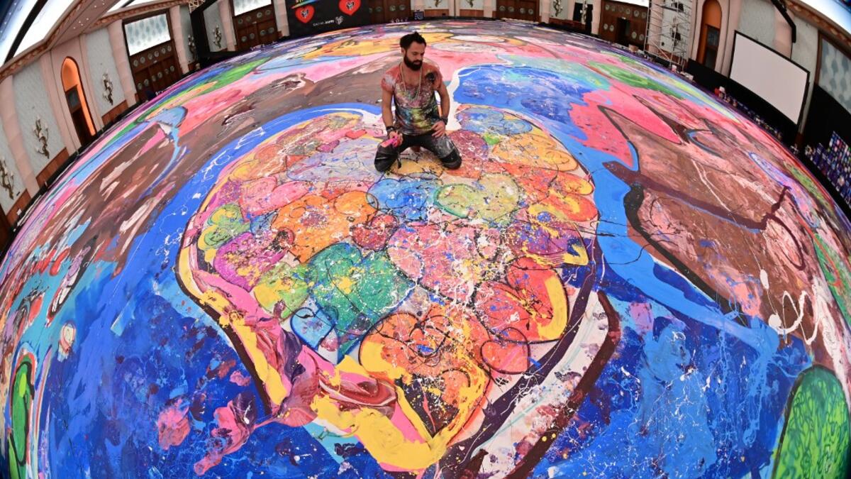 Contemporary British artist Sacha Jafri (C) stands on his record-breaking painting entitled 'The Journey of Humanity' on September 23, 2020, in the Emirati city of Dubai. The painting, which measures the size of two football fields, can be seen at a hotel in Dubai, where Jafri spent months of lockdown due to the coronavirus pandemic. The gigantic artwork is part of his project 'Humanity Inspired' and with it he hopes to raise 30 million USD to fund health and education initiatives for children living in pov