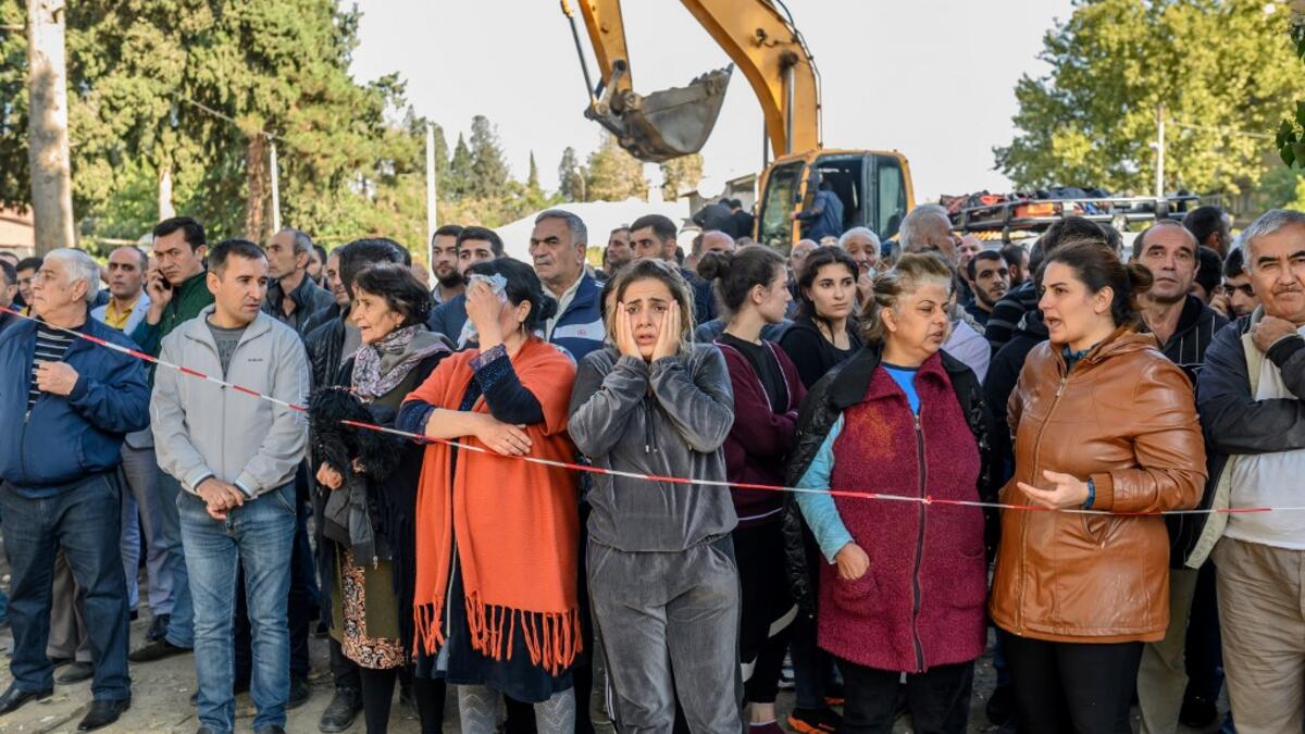People stand behind caution tape as rescuers search for victims or survivors at the blast site hit by a rocket during the fighting between Armenia and Azerbaijan over the breakaway region of Nagorno-Karabakh, in the city of Ganja, Azerbaijan, on October 11, 2020. Bulent Kilic / AFP