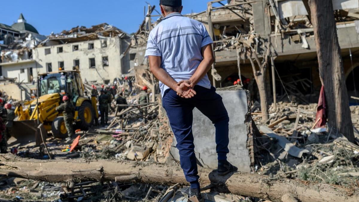 A man looks at rescuers searching for victims or survivors at the blast site hit by a rocket during the fighting between Armenia and Azerbaijan over the breakaway region of Nagorno-Karabakh, in the city of Ganja, Azerbaijan, on October 11, 2020. Bulent Kilic / AFP