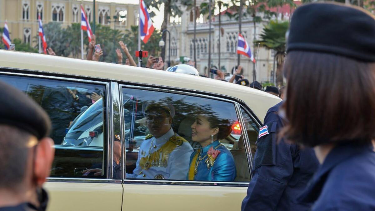 Thailand's Queen Suthida (C) and Prince Dipangkorn Rasmijoti (centre L) react inside a royal motorcade as it drives past a pro-democracy rally, as anti-government protesters (back) hold up their three-finger salute, in Bangkok on October 14, 2020. Teera NOISAKRAN / AFP