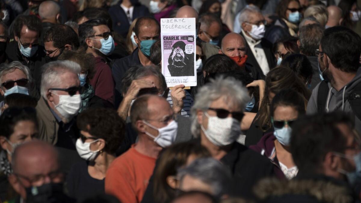 A person holds the front page of French satirical weekly Charlie Hebdo reading "Liberty, tolerance and equality" as people gather on the Vieux Port in Marseille on October 18, 2020, in homage to history teacher Samuel Paty two days after he was beheaded by an attacker who was shot dead by policemen. CHRISTOPHE SIMON / AFP