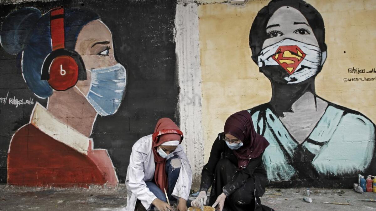Palestinian students dip their brushes as they paint murals of mask-clad girls in Gaza City on October 22, 2020, amid the novel coronavirus pandemic crises. Mohammed ABED / AFP
