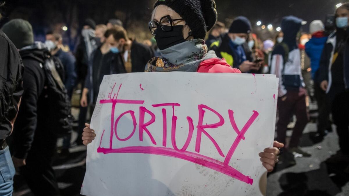 A protestor blocked by riot police guarding the house of Jaroslaw Kaczynski, leader of Poland's ruling Law and Justice party (PIS)holds a poster reading "torture" during a demonstration against a decision by the Constitutional Court on abortion law restriction,in Warsaw on October 23, 2020. Wojtek RADWANSKI / AFP