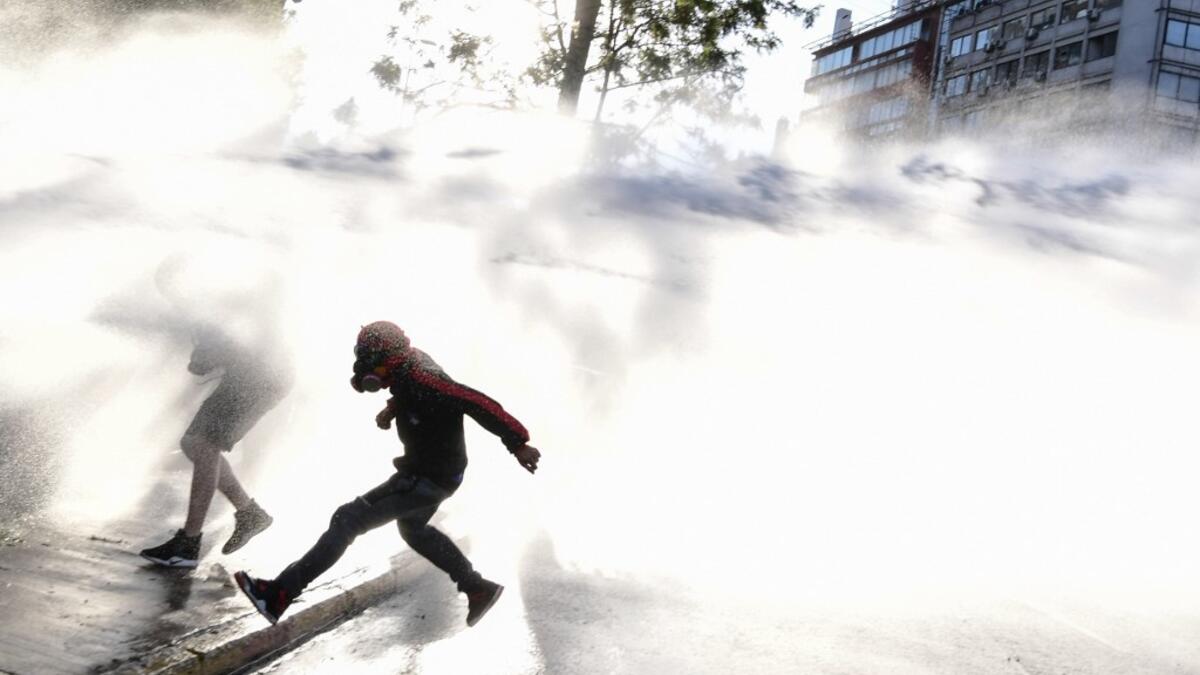 Demonstrators are sprayed with water canons by riot police in a protest against Chilean President Sebastian Pinera's government during the constitutional referendum voting day at Plaza Italia square in Santiago on October 25, 2020. A year to the day after more than one million people thronged downtown Santiago in the biggest Chile's social uprising, Chileans vote Sunday on whether to change the country's dictatorship-era constitution seen as underpinning the nation's glaring inequalities. Martin BERNETTI /