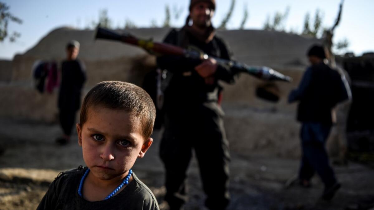 In this photo taken on September 27, 2020, a young boy looks at the camera as a policeman holding a rocket-propelled grenade (RPG) stands behind in a house at Deh Qubad village in Maiwand district of Kandahar province. The dry and dusty village of Aziz Abad in Maiwand district sits on the frontline of Afghanistan's war and is currently under government control -- but only just. WAKIL KOHSAR / AFP