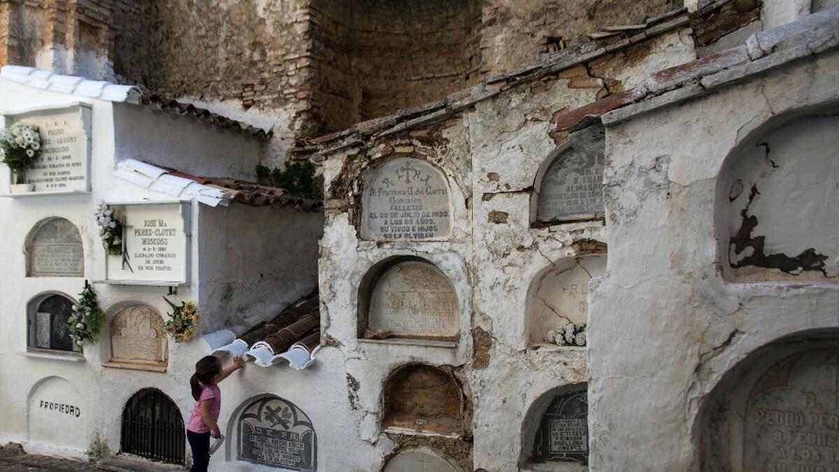 A girl touches a grave at the Cemetery of Villaluenga del Rosario near Cadiz on All Saints' Day on November 1, 2020. The Cemetery of Villaluenga is built on the ruins of the El Salvador Church which was burnt during the war of independence. CRISTINA QUICLER / AFP