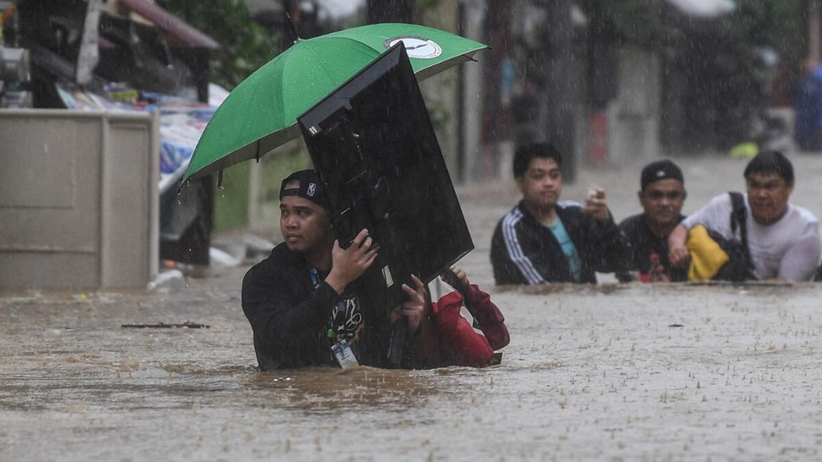 A man (L) carries a television as residents make their way through a flooded street to shelter after Typhoon Vamco hit the area in Marikina City, suburban Manila on November 12, 2020. Ted ALJIBE / AFP