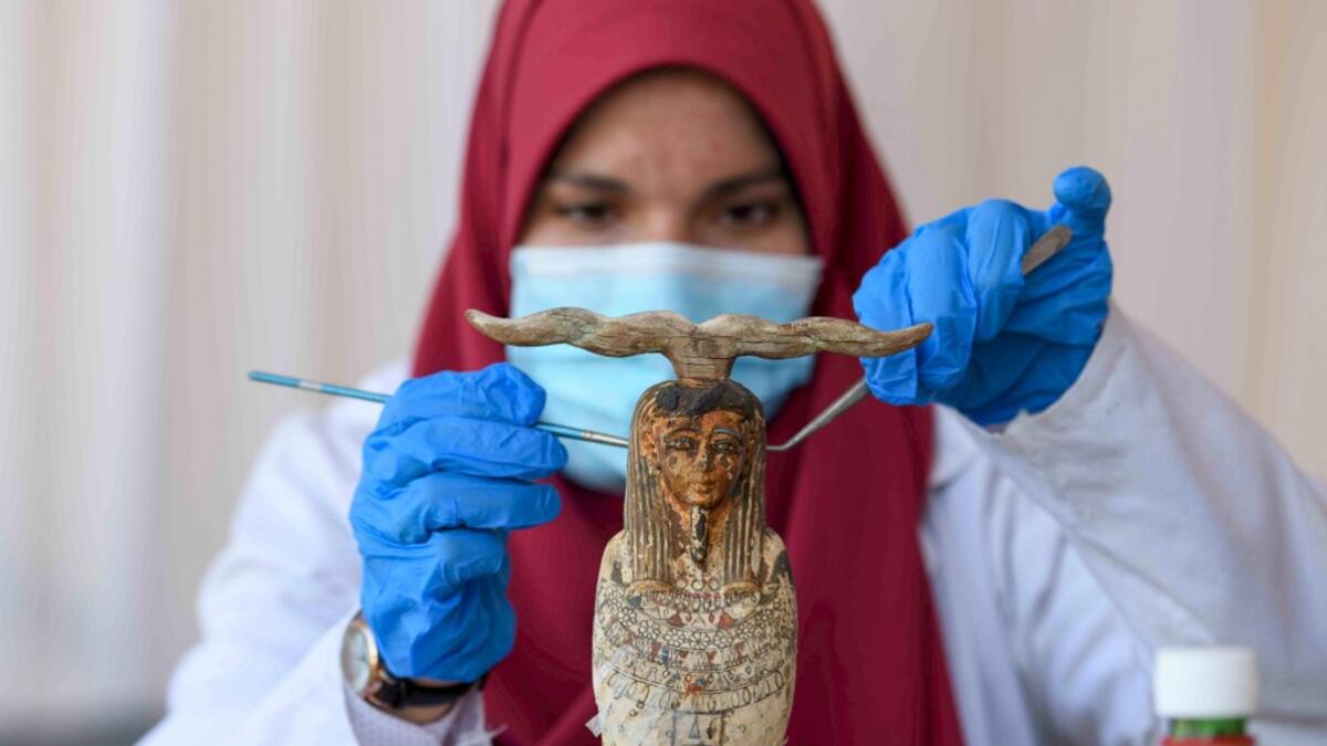 An archaeologist cleans a statue during the unveiling of an ancient treasure trove of more than a 100 intact sarcophagi, at the Saqqara necropolis 30 kms south of the Egyptian capital Cairo, on November 14, 2020. Egypt announced the discovery of an ancient treasure trove of more than a 100 intact sarcophagi, the largest such find this year. The sealed wooden coffins, unveiled on site amid fanfare, belonged to top officials of the Late Period and the Ptolemaic period of ancient Egypt. They were found in thre