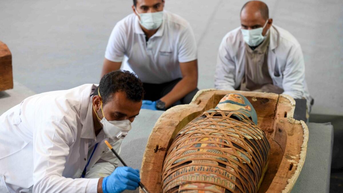 Archaeologists inspect a mummy, wrapped in a burial shroud adorned with brightly coloured hieroglyphic pictorials, during the unveiling of an ancient treasure trove of more than a 100 intact sarcophagi, at the Saqqara necropolis 30 kms south of the Egyptian capital Cairo, on November 14, 2020. Egypt announced the discovery of an ancient treasure trove of more than a 100 intact sarcophagi, the largest such find this year. The sealed wooden coffins, unveiled on site amid fanfare, belonged to top officials of