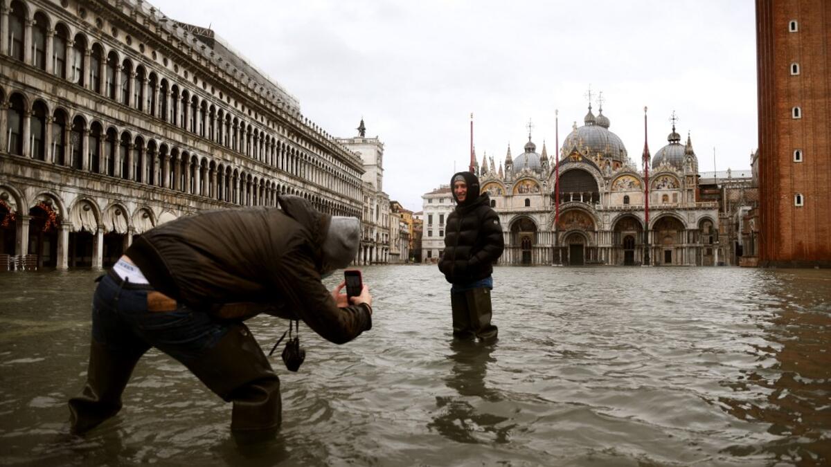 People talk photos in the middle of a flooded St. Mark's Square on December 8, 2020 in Venice following a high tide "Alta Acqua" event following heavy rains and strong winds, and the mobile gates of the MOSE Experimental Electromechanical Module that protects the city of Venice from floods, were not lifted ANDREA PATTARO / AFP