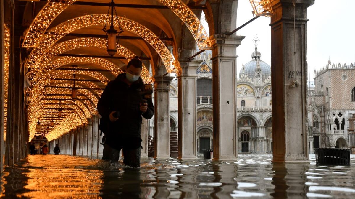 A man walks across an arcade by a flooded St. Mark's Square on December 8, 2020 in Venice following a high tide "Alta Acqua" event following heavy rains and strong winds, and the mobile gates of the MOSE Experimental Electromechanical Module that protects the city of Venice from floods, were not lifted ANDREA PATTARO / AFP