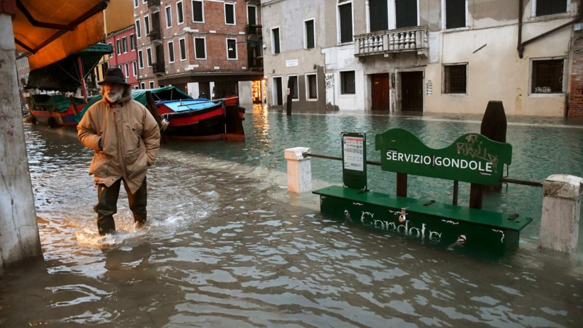 A man walks across a flooded canal on December 8, 2020 in Venice following a high tide "Alta Acqua" event following heavy rains and strong winds, and the mobile gates of the MOSE Experimental Electromechanical Module that protects the city of Venice from floods, were not lifted ANDREA PATTARO / AFP