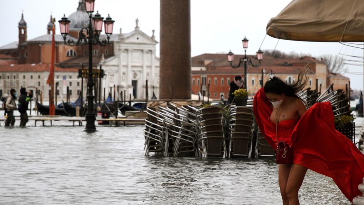 A view shows a model holding her dress on a flooded St. Mark's Square on December 8, 2020 following a high tide "Alta Acqua" event following heavy rains and strong winds, and the mobile gates of the MOSE Experimental Electromechanical Module that protects the city of Venice from floods, were not lifted. ANDREA PATTARO / AFP