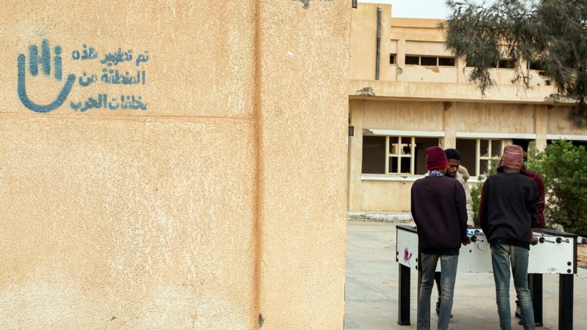 Youths play table football (foosball) outside by abandoned buildings, with graffiti nearby reading in Arabic "this zone has been cleared of the remains of war", in the city of Tawergha, some 200 kilometres (125 miles) east of Libya's capital close to the port city of Misrata, on December 12, 2020. When Libyan dictator Moamer Kadhafi was toppled, people took revenge on those they saw as his supporters -- including the entire town of Tawergha, whose 40,000 residents were forced to flee. Now, almost a decade l