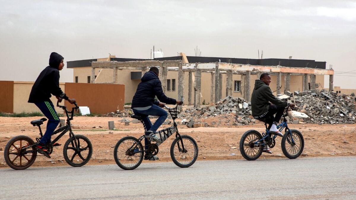 Youths play table football (foosball) outside by abandoned buildings, with graffiti nearby reading in Arabic "this zone has been cleared of the remains of war", in the city of Tawergha, some 200 kilometres (125 miles) east of Libya's capital close to the port city of Misrata, on December 12, 2020. When Libyan dictator Moamer Kadhafi was toppled, people took revenge on those they saw as his supporters -- including the entire town of Tawergha, whose 40,000 residents were forced to flee. Now, almost a decade l