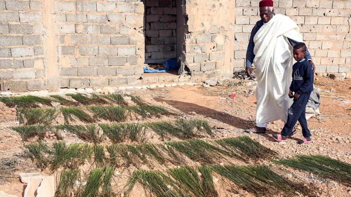 Mahmud Abu al-Habel, a 70-year-old resident of Tawergha who was among the first who returned to the city after fleeing in the aftermath of the toppling of Kadhafi, stands outside a damaged house with a boy in the city of Tawergha, some 200 kilometres (125 miles) east of Libya's capital close to the port city of Misrata, on December 12, 2020. When Libyan dictator Moamer Kadhafi was toppled, people took revenge on those they saw as his supporters -- including the entire town of Tawergha, whose 40,000 resident