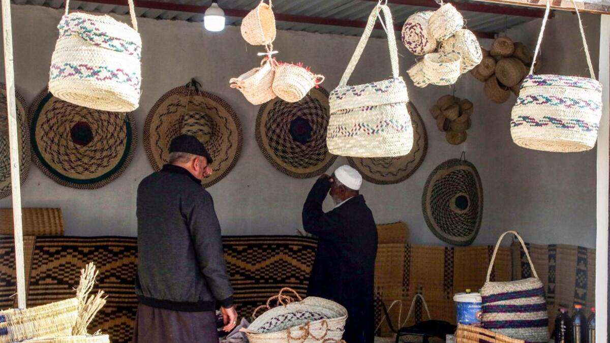 People inspect palm wicker products on display, made by Haleema Mohamed, one of the residents who returned to the city of Tawergha after fleeing in the aftermath of the toppling of Kadhafi, sits making palm wicker products at a home in Tawergha, some 200 kilometres (125 miles) east of Libya's capital close to the port city of Misrata, on December 12, 2020. When Libyan dictator Moamer Kadhafi was toppled, people took revenge on those they saw as his supporters -- including the entire town of Tawergha, whose