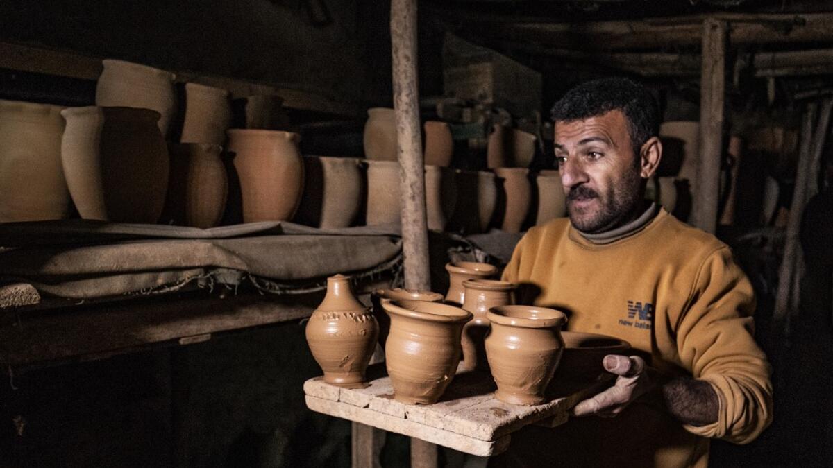 The son of Syrian-Armenian potter Misak Antranik Petros carries vases for drying at his father's workshop located inside an ancient mud-brick house near the city of Qamishli in Syria's northeastern Hasakeh province, on December 19, 2020. Petros was only a teenager when he had to take over for his sick father and become the main potter of the family. He has since become a master of the craft, and is keen to pass his skills on.  Delil SOULEIMAN / AFP