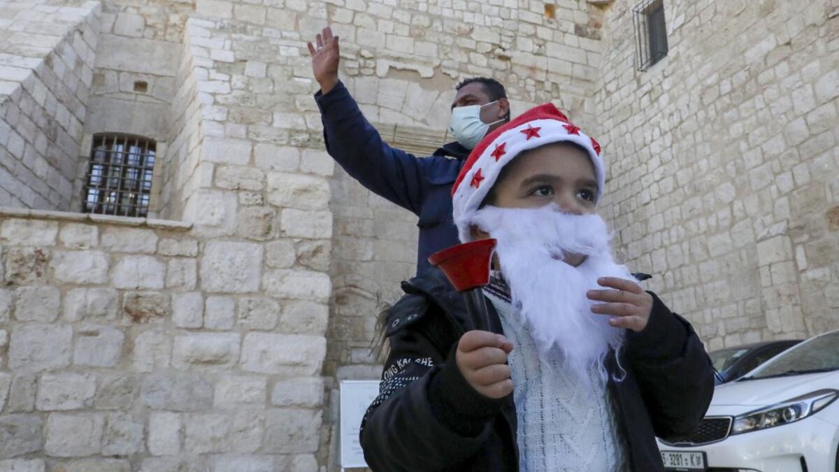 A Palestinian wearing a Santa Claus beard and hat rings a bell outside the Church of the Nativity, in the West Bank city of Bethlehem, on December 20, 2020 after it was re-opened for prayers following strict COVID-19 restrictions. HAZEM BADER / AFP