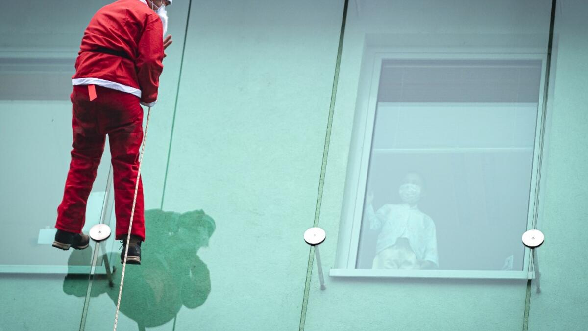 A man dressed as a Santa Claus waves to a child as he descends from the roof of the paediatric clinic in Ljubljana, Slovenia on December 21, 2020. Jure Makovec / AFP