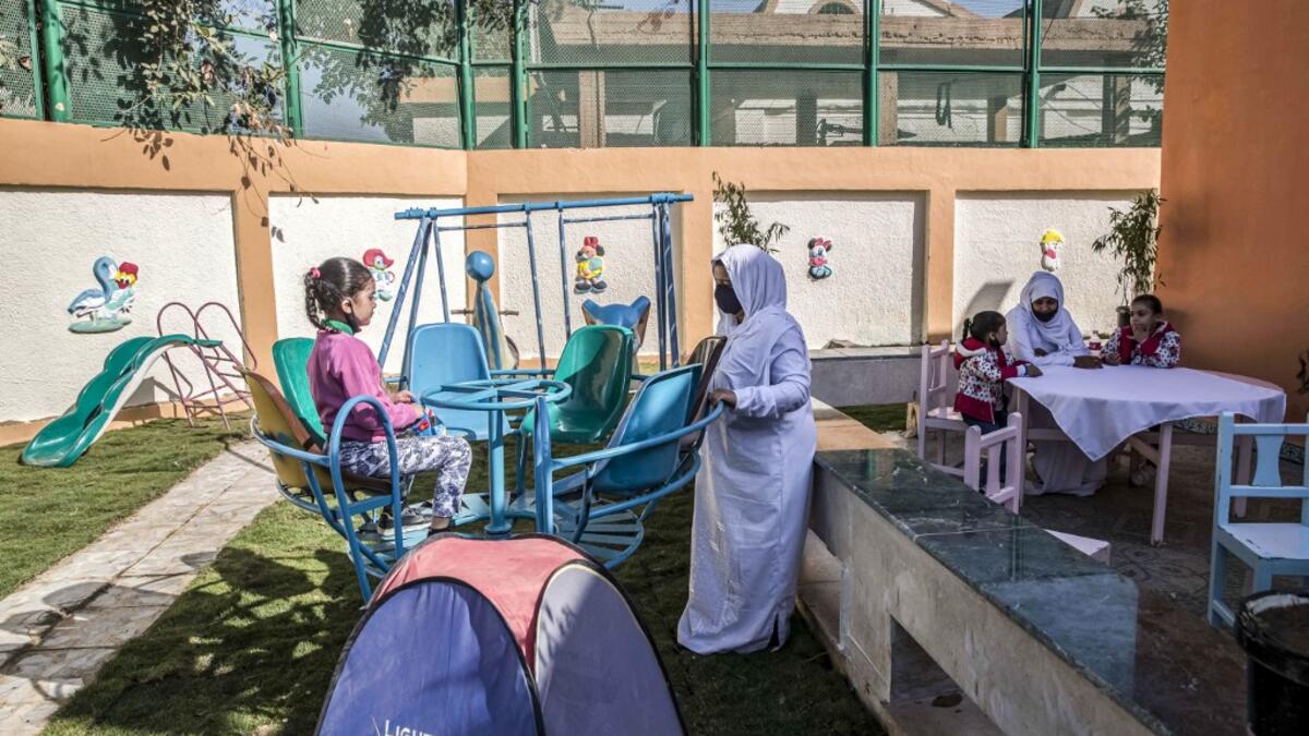 This picture taken during a government-guided tour on December 27, 2020 shows an inmate, mask-clad due to the COVID-19 coronavirus pandemic, pushing a child on a swing at the recreational area of al-Qanatir women's prison, at the tip of the Nile delta in Qalyoubiya province, about 30 kilometres north of Egypt's capital. Khaled DESOUKI / AFP
