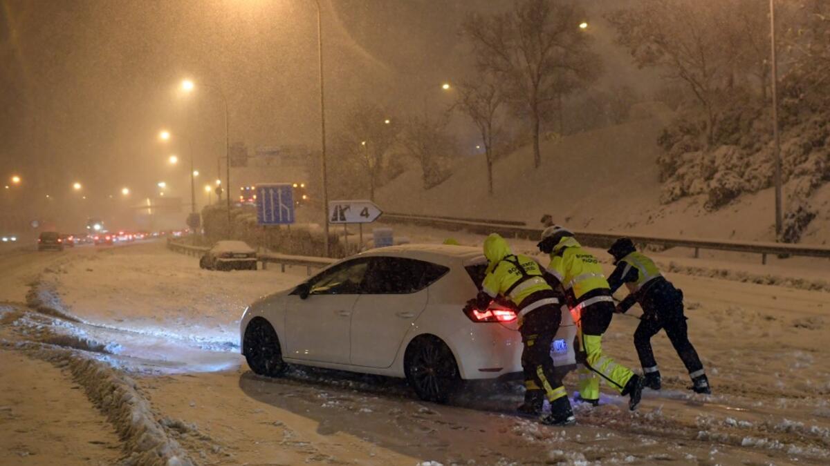 Firefighters push a vehicle stuck in the M30 ringroad in Madrid due to a heavy snow storm on January 8, 2021. Heavy snow fell across much of Spain today, leaving huge areas blanketed in white as Storm Filomena brought wintry weather not seen in decades to the Iberian peninsula. The intense snow cut off Madrid's two ringroads, the M30 and the M40, and a red alert was declared in the city centre where police were struggling to help people stranded in vehicles. OSCAR DEL POZO / AFP