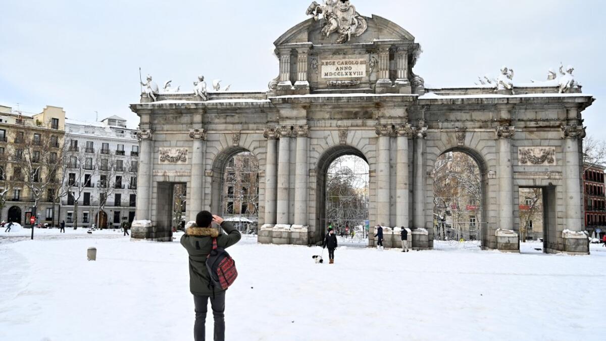 People take pictures in front of the Puerta de Alcala in Madrid on January 10, 2021. Snowstorms in Spain left three people dead and caused chaos across much of the country, trapping motorists and shutting down the capital's air and rail links. Gabriel BOUYS / AFP