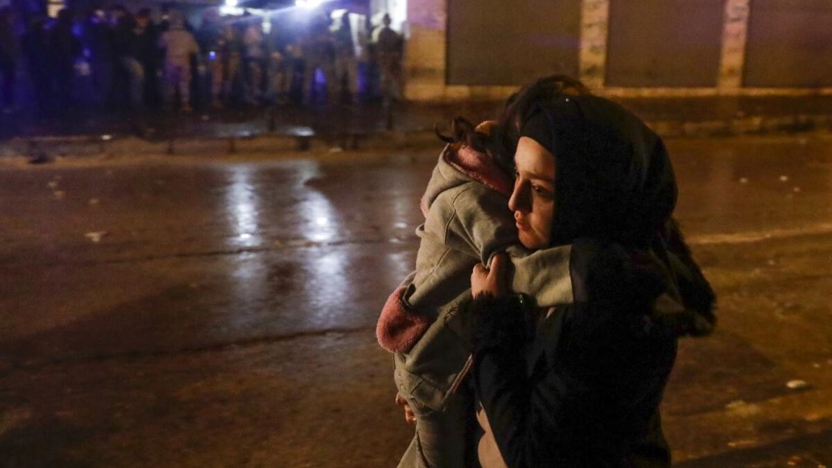 A woman crosses a street with her child during clashes between security forces and anti-government protesters in the northern city of Tripoli, on January 29, 2021. More than 400 people have been wounded in northern Lebanon this week in clashes between security forces and protesters angered by a coronavirus lockdown they say is starving them. JOSEPH EID / AFP