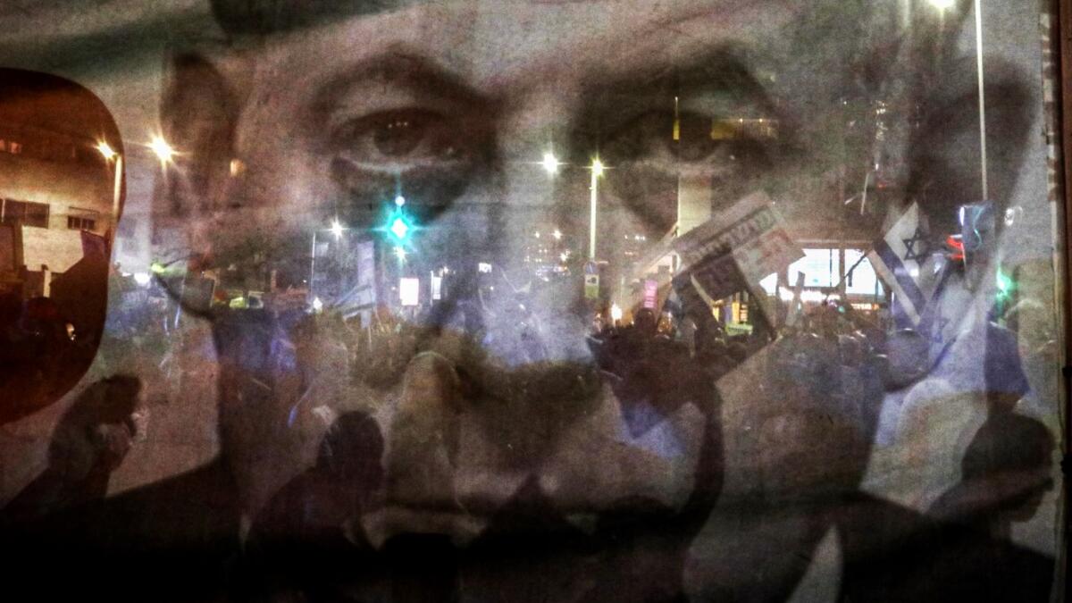 In this file photo taken on August 11, 2018, silhouettes of demonstrator are seen through a giant poster depicting Israeli Prime Minister Benjamin Netanyahu as Arab Israelis and their supporters march in a rally to protest against the 'Jewish Nation-State Law' in the Israeli coastal city of Tel Aviv. Israel's Prime Minister Benjamin Netanyahu returns to court on February 8, 2021 to formally respond to the corruption charges filed against him, as his trial enters an intensified phase six weeks before he face